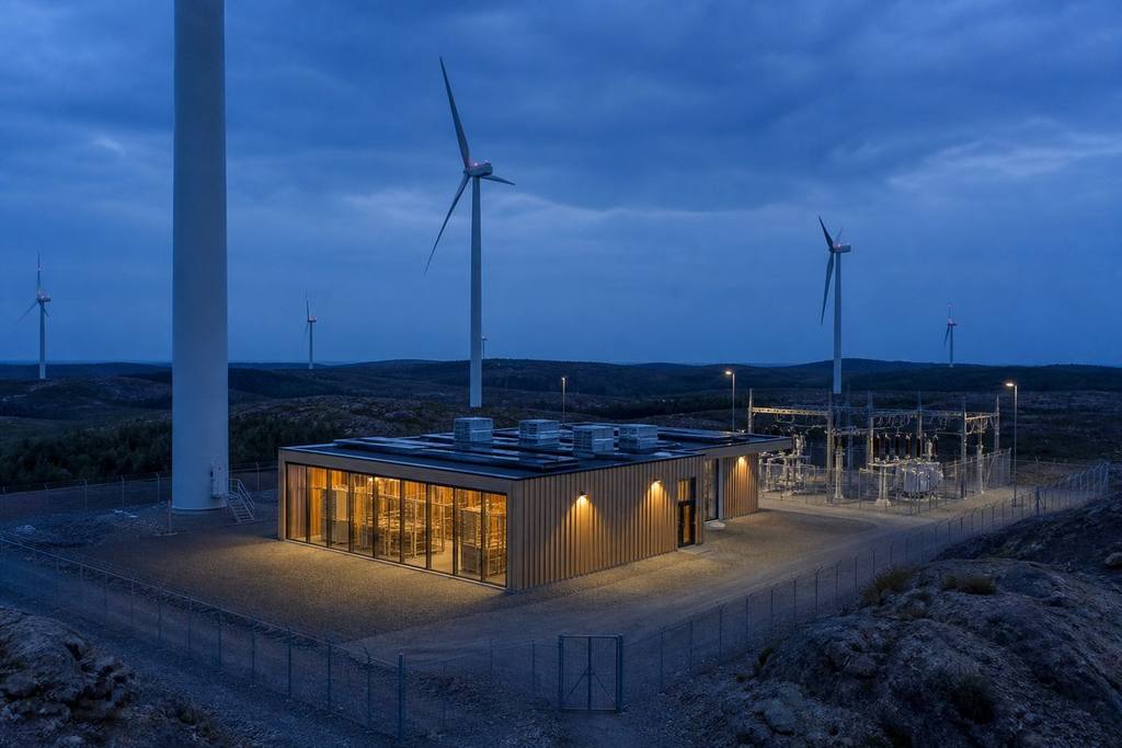 Visualization of a Compute hall on a fenced pad inside a wind park, at the foot of a turbine. Visualization, not a photograph of an operating site.